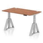 The picture shows a modern office desk with a walnut top and silver legs. It has the dimensions of 1400 x 800mm and features a dynamic sit-stand function, allowing for adjustable height. The desk also includes built-in cable ports and a unique piste foot design, providing additional support and stability.