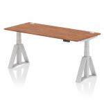 This photo features a dynamic sit stand and height adjustable desk, measuring 1800 x 800mm. It has a walnut top with cable ports and sleek silver legs, complete with a Piste foot. The desk is fully adjustable for optimal ergonomics and functionality.