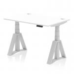 The photograph shows a sleek white desk with silver legs and a spacious 1200 x 800mm top. The desk is equipped with cable ports for easy organization and a piste foot for adjustable height. It can be used as a sit-stand desk for a dynamic work environment.