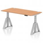 The image shows a sleek and modern office desk with a 1600 x 800mm oak top and silver legs. It features dynamic sit stand and height adjustable capabilities, as well as cable ports and a piste foot for added functionality. The overall design exudes a professional and ergonomic feel.