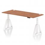 The photo shows a sleek and modern dynamic sit stand and height adjustable desk with a walnut top and white leg, equipped with cable ports and a piste foot for stability. Its 1800 x 800mm size makes it perfect for any office space.