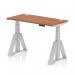 The photograph shows a dynamic sit stand and height adjustable desk measuring 1200 x 600mm. The desk features a walnut top with cable ports, supported by a silver leg with a piste foot. The desk is perfect for a modern office setting and allows for comfortable and ergonomic work conditions.