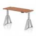 This picture shows a sleek, modern, and versatile dynamic sit-stand height adjustable desk. The desk has a spacious 1400 x 600mm walnut top with cable ports for convenient organization. The silver legs add a touch of elegance, and the piste foot adds stability and support.