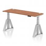 The image shows a sleek, modern office desk with a walnut top and silver legs. The desk is height adjustable and also features a dynamic sit-stand feature. It measures 1600mm by 600mm and has built-in cable ports for easy organization. The unique Piste Foot adds a touch of style and functionality to this versatile desk.
