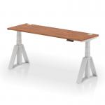 The photo shows a sleek and modern office desk with a 1800x600mm walnut top, supported by silver legs and a piste foot. The desk is height adjustable and features cable ports for a clutter-free workspace. Its dynamic design allows for easy transition between sitting and standing positions.
