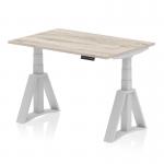 The photograph showcases a sleek and modern office desk measuring 1200 x 800mm. The grey oak top complements the silver legs and Piste foot, creating a sophisticated look. It is a dynamic sit-stand desk that can be easily adjusted to suit the users needs.