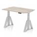 The photograph showcases a sleek and modern office desk measuring 1200 x 800mm. The grey oak top complements the silver legs and Piste foot, creating a sophisticated look. It is a dynamic sit-stand desk that can be easily adjusted to suit the users needs.
