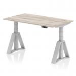 The image features a sleek and modern 1400 x 800mm height adjustable office desk in a grey oak top with silver legs and a piste foot. The desk is equipped with a dynamic sit stand function, allowing for a more ergonomic work experience. The adjustable height feature provides versatility for different users and preferences.