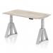 The image features a sleek and modern 1400 x 800mm height adjustable office desk in a grey oak top with silver legs and a piste foot. The desk is equipped with a dynamic sit stand function, allowing for a more ergonomic work experience. The adjustable height feature provides versatility for different users and preferences.