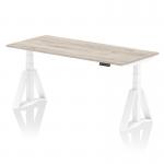 The photo shows a sleek and modern office desk with a durable grey oak top and a sturdy white leg. It features a dynamic sit-stand function and can be adjusted to a height of 1800 x 800mm. The addition of a piste foot provides extra stability for ergonomic use.