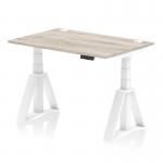 This photo features a sleek and modern office desk with a grey oak top and white legs. The desk is 1200 x 800mm and is height adjustable, allowing for dynamic sit and stand options. It also includes cable ports and a piste foot for added convenience.