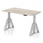 This sleek and modern desk features a grey oak top with cable ports for easy organization, silver legs, and a piste foot for added stability. Its dynamic sit stand capabilities and height adjustability make it a versatile and ergonomic addition to any office space.
