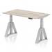 This sleek and modern desk features a grey oak top with cable ports for easy organization, silver legs, and a piste foot for added stability. Its dynamic sit stand capabilities and height adjustability make it a versatile and ergonomic addition to any office space.