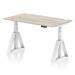 The photo features a sleek grey oak top on a height adjustable office desk, with white legs and a piste foot. The desk also includes cable ports for a clean and organized workspace. The adjustable design allows for a dynamic sit-stand experience, promoting improved ergonomics and productivity.