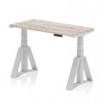 This photograph showcases a modern office desk with a sleek grey oak top and a height adjustable feature. The silver leg and piste foot add a touch of elegance, while cable ports ensure a clutter-free workspace. The desk measures 1200 x 600mm and features a dynamic sit stand option, making it perfect for a versatile and productive work environment.
