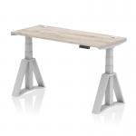 This picture features a sleek and modern dynamic sit stand and height adjustable desk. The desk measures 1400 x 600mm and has a grey oak top with cable ports and silver legs. The desk also includes a piste foot for added stability.