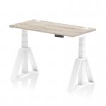 The photograph shows a modern and versatile desk with a grey oak top and white leg. It is equipped with cable ports and a piste foot for added convenience. Ideal for creating a dynamic work environment, this desk offers both sit and stand options and can be easily adjusted in height.