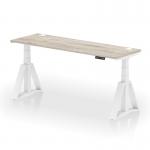 The photo shows a modern and sleek dynamic sit stand and height adjustable office desk, measuring 1800 x 600mm. Its grey oak top contrasts beautifully with its white leg and piste foot, creating a stylish look. Cable ports are conveniently placed for easy organization. Perfect for any productive workspace.