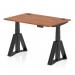 The photo shows a sleek and modern office desk with a walnut top and black legs. The desk is 1200 x 800mm and features a height adjustable design, along with cable ports and a piste foot for added functionality. It exudes a dynamic and professional feel, perfect for any modern workspace.