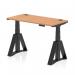 This photograph shows a dynamic sit stand and height adjustable desk with an oak top and black legs. The desk measures 1200 x 600mm and features cable ports and a piste foot.