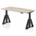 The image shows a sleek and modern office desk with a grey oak top and black legs. It features a dynamic sit stand and height adjustable function, measuring 1600 x 800mm. The design is completed with a piste foot for added stability.