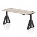 This photo showcases a large, modern office desk with a grey oak top and black adjustable legs. The surface is equipped with cable ports for easy organization. The unique feature is the piste foot, allowing for dynamic sit stand options. Perfect for a versatile and functional workspace.
