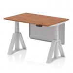 The photo shows a modern and versatile workspace with a dynamic sit-stand and height adjustable desk. The desk has a walnut top and silver legs, as well as a silver steel modesty panel and piste foot. This desk offers flexibility and functionality in any office setting.