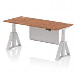 This photo features a sleek and modern office desk measuring 1800 x 800mm. The desk is height adjustable and boasts a walnut top with cable ports, silver legs, and a piste foot for added stability. The silver steel modesty panel adds a touch of style to this dynamic sit stand desk.