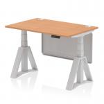 The photograph shows a sleek and modern office desk with a 1200 x 800mm oak top that can be adjusted in height. It features a silver leg with cable ports, a silver steel modesty panel, and a piste foot. This dynamic sit stand desk is perfect for creating a customizable and ergonomic workspace.