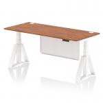 The photo shows a modern office desk that is 1800 x 800mm in size and features a walnut top with cable ports. The white leg and steel modesty panel give a clean and sleek look, while the piste foot adds a touch of uniqueness. The desk is also height adjustable, perfect for a dynamic sit-stand work setup.