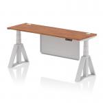 The photo shows a modern office desk that is 1800mm x 600mm in size. It has a sleek walnut top and silver legs with a matching steel modesty panel. The desk is height adjustable and features cable ports for organization. A piste foot adds a stylish touch to this dynamic sit stand desk.