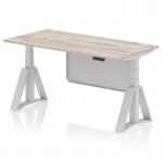 This photograph features a sleek and modern office desk, sized at 1600 x 800mm, with a grey oak top and silver legs. The desk is height adjustable and includes cable ports, as well as a silver steel modesty panel and piste foot for added support.