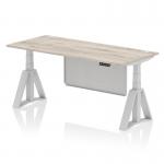 The image shows a sleek and modern 1800 x 800mm grey oak top desk with a silver leg and silver steel modesty panel. The desk is height adjustable, with cable ports for organization and a piste foot for stability. It exudes a sense of flexibility, style and versatility for any office setting.