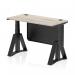 This photograph captures a sleek and modern office desk with a grey oak top and black steel legs. The desk is height adjustable and features cable ports, a modesty panel, and a piste foot for added stability. Its compact 1200 x 600mm size makes it perfect for any dynamic sit-stand work environment.