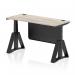 This picture features a sleek grey oak top desk with a black steel modesty panel and cable ports. The desk is supported by a black leg with a piste foot and has the ability to adjust in height for a comfortable sitting or standing position.