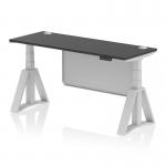 This photo features a sleek, modern office desk with a black top and silver legs. The desk is equipped with a height adjustable feature and cable ports for convenience. A silver steel modesty panel and piste foot add an extra touch of style to this dynamic sit stand desk.