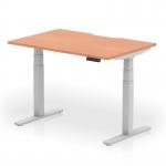 The picture shows a modern, versatile office desk with a sleek beech top and silver legs. Its scalloped edge adds a touch of sophistication. The desk is adjustable in height and can be used for sitting or standing, making it ideal for a dynamic work environment.