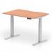 The picture shows a modern, versatile office desk with a sleek beech top and silver legs. Its scalloped edge adds a touch of sophistication. The desk is adjustable in height and can be used for sitting or standing, making it ideal for a dynamic work environment.