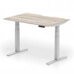 The photograph features the sleek and modern design of a Dynamic Sit Stand and Height Adjustable Desks Air in a stylish grey oak top with a silver leg. The scalloped edge adds a unique touch to the 1200 x 800mm workspace, making it a practical and versatile option for any office.