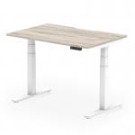 This image shows a dynamic sit stand desk with a 1200 x 800mm grey oak top and white legs. The desk has a scalloped edge and can be adjusted to different heights, making it suitable for any office space.