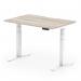 This image shows a dynamic sit stand desk with a 1200 x 800mm grey oak top and white legs. The desk has a scalloped edge and can be adjusted to different heights, making it suitable for any office space.