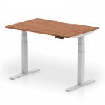 This picture shows a sleek and modern dynamic sit-stand desk with a scalloped edge, measuring 1200 x 800mm. The desk has a walnut top and silver legs, giving it a professional and stylish look. It is height adjustable, allowing for a dynamic work environment.