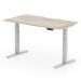 The image shows a stylish and modern grey oak top office desk with a scalloped edge, sitting on top of a sleek silver leg. The desk is equipped with an adjustable mechanism, allowing the user to switch between sitting and standing positions for a more dynamic work experience. Measuring 1400 x 800mm, this desk is perfect for any office space.
