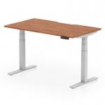 This photo captures a modern, sleek Dynamic Sit Stand and Height Adjustable Desk. The desk features a Walnut top with a scalloped edge and a silver leg, providing a stylish and functional workspace.
