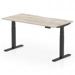 This photo is a close-up of a sleek grey oak top with a scalloped edge placed on top of a dynamic sit stand and height adjustable desk. The black legs provide a sturdy base for the desk, which measures 1600 x 800mm.