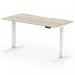 The picture shows a sleek and modern office desk with a grey oak top and white legs. The desk has a scalloped edge design and can be adjusted to different heights, making it suitable for both sitting and standing. It measures 1600 x 800mm and is perfect for a dynamic and adaptable workspace.
