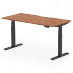 This photograph features a sleek and modern Dynamic Sit Stand and Height Adjustable Desk. The desk size is 1600 x 800mm with a scalloped edge design. The top is made of walnut while the legs are sleek black. The desk is fully height adjustable, making it perfect for any office space.