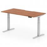 This picture features a sleek and modern Dynamic Sit Stand and Height Adjustable Desk, measuring 1600 x 800mm with a scalloped edge design. The desk has a stylish Walnut top and a silver leg, creating a professional and functional addition to any office space.