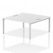 Two people are seated at a sleek white bench desk with silver frames. The dynamic design of the bench encourages collaboration and productivity in a modern office setting.