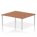 This photograph features a sleek and modern office bench desk with a silver frame and walnut top. It is designed for two people and offers a dynamic and efficient working space. The clean lines and simple design make it a stylish addition to any office.